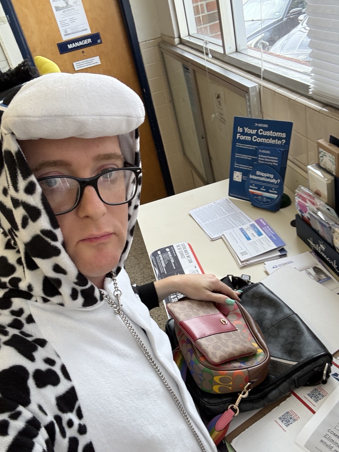 Veronica in a black-and-white cow costume at a post office counter with bags